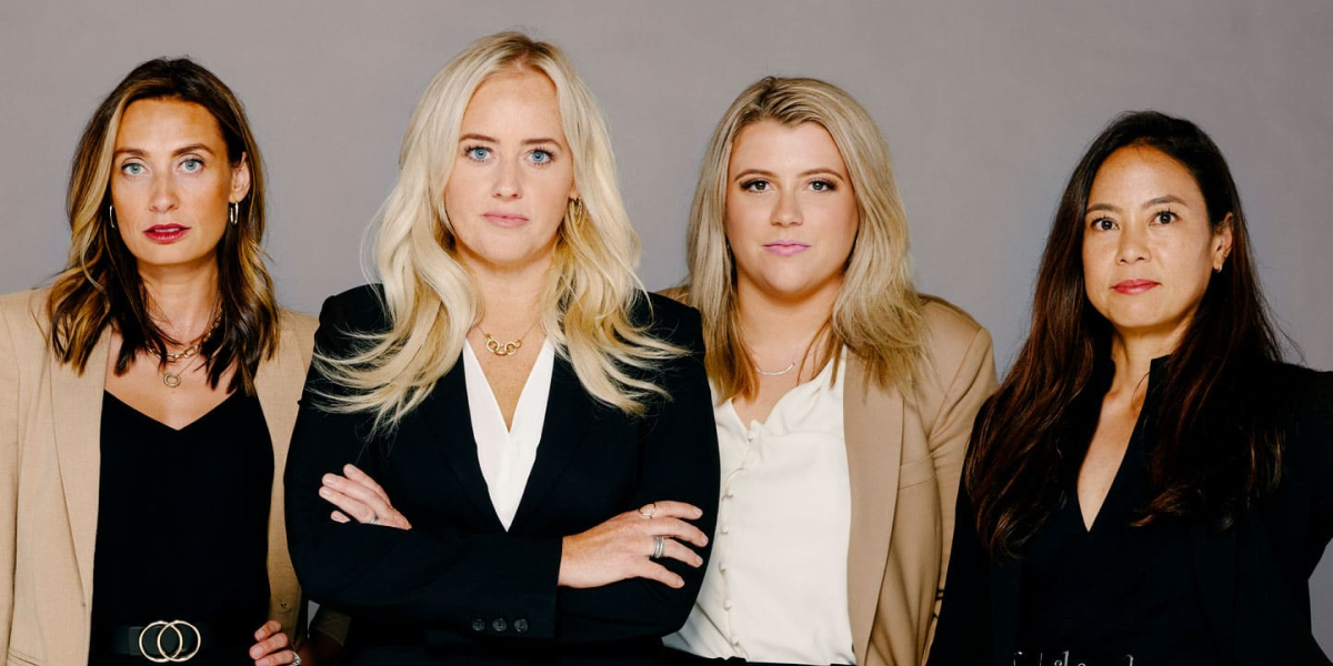 four women standing shoulder to shoulder looking into camera